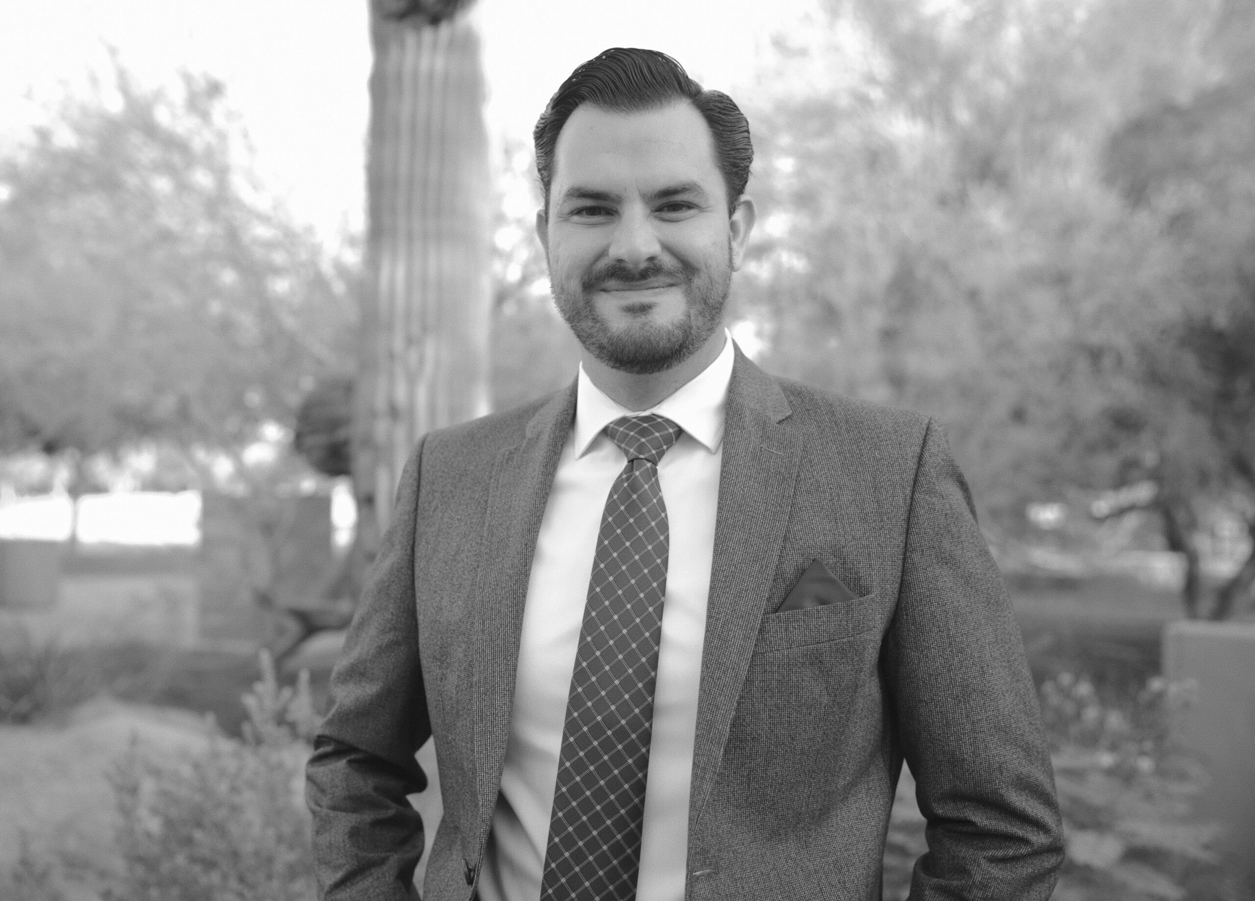 Black and white picture of Carlos Alfaro in a suit standing in front of a cactus.
